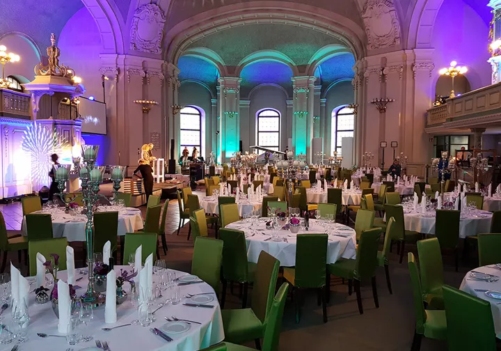 Large hall with set tables, chairs and purple lights on the walls